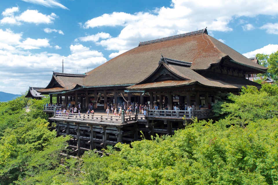 Kiyomizu-dera’s wooden main hall and terrace surrounded by green trees in Kyoto.